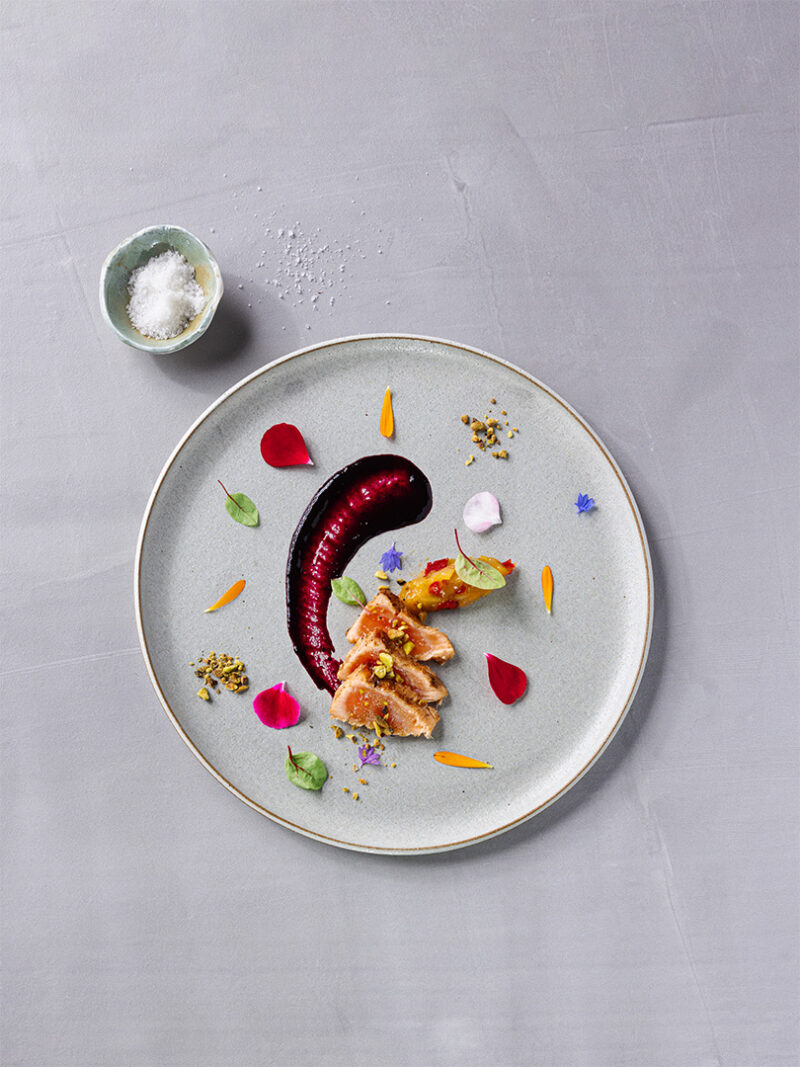 Plat de saumon mi-cuit dressé avec purée de betterave, pétales comestibles et garnitures.