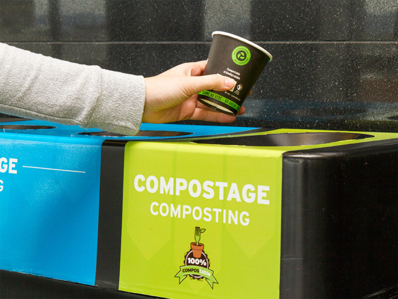Main déposant un gobelet compostable dans un bac vert de compostage au Centre des congrès.