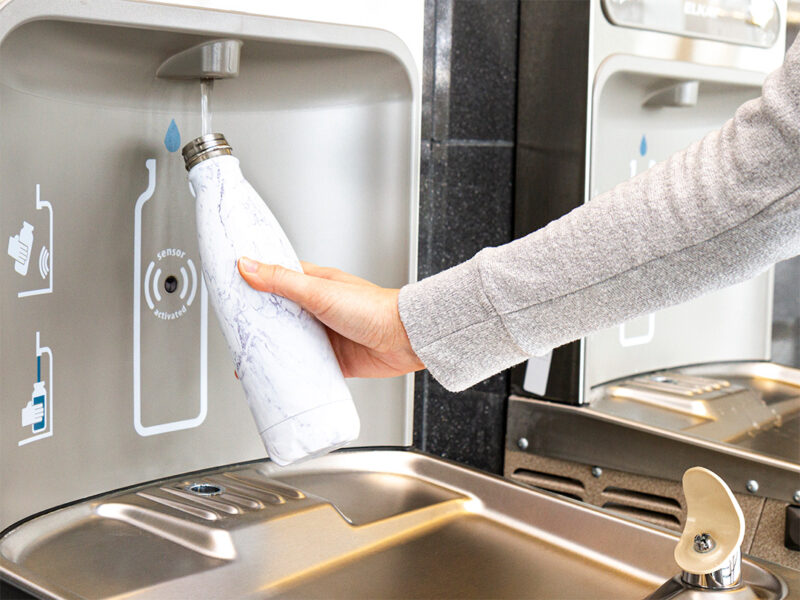 Main remplissant une bouteille réutilisable à une station de remplissage d’eau sans contact.